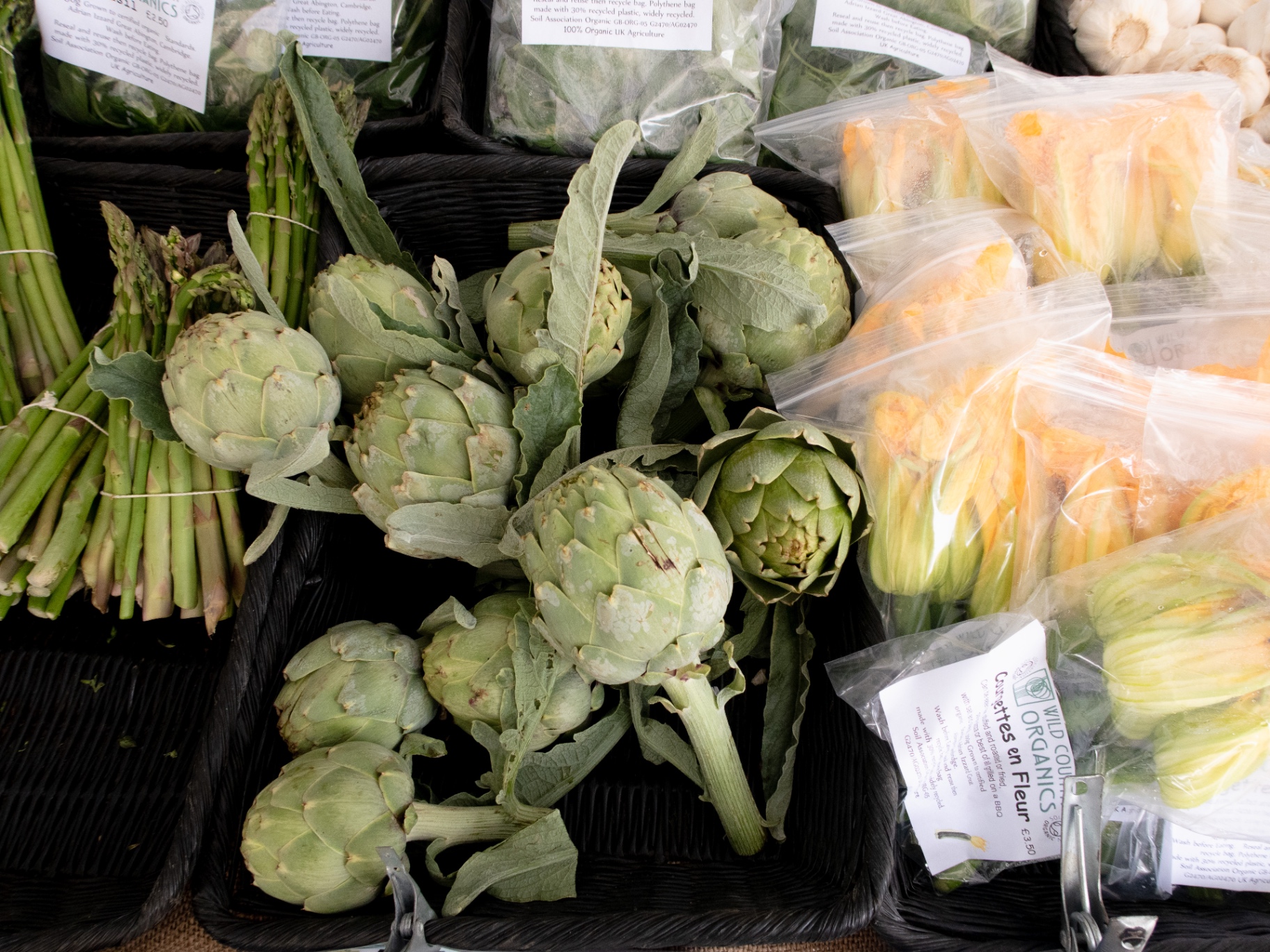 Fresh produce at a market stall with artichokes, asparagus and courgette flowers